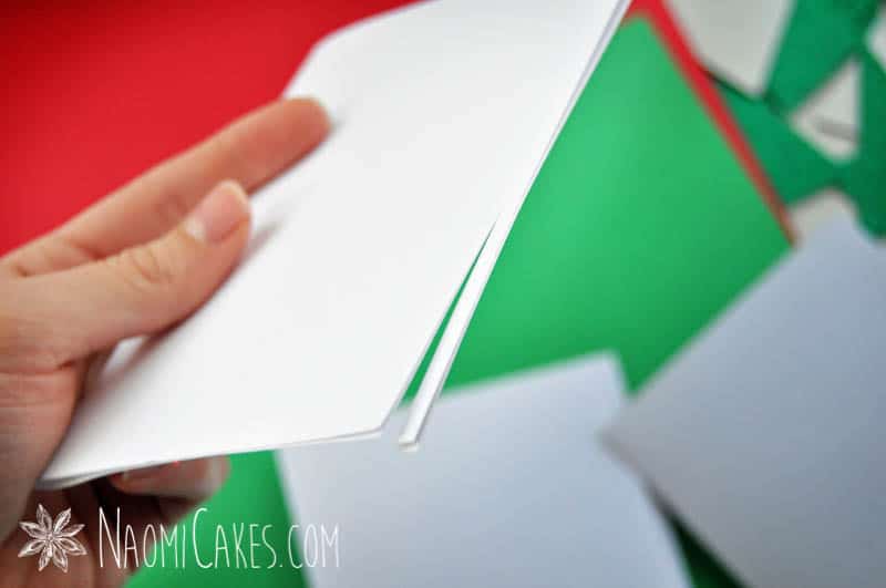 a woman's hand holding a piece of white card stock with the edge partially trimmed away