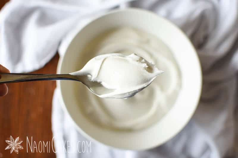 overhead view of a spoonful of royal icing over a bowl sitting on a table with a white cloth