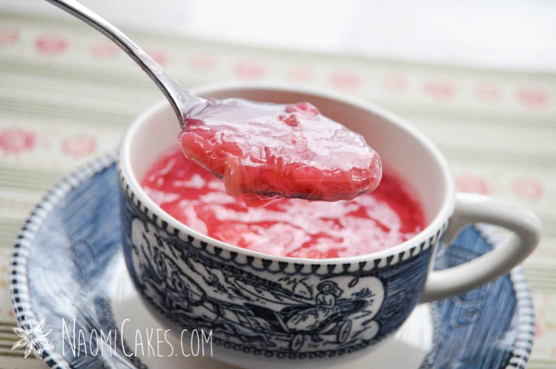 spoon showing pink rhubarb sauce in a tea cup on patterned paper background