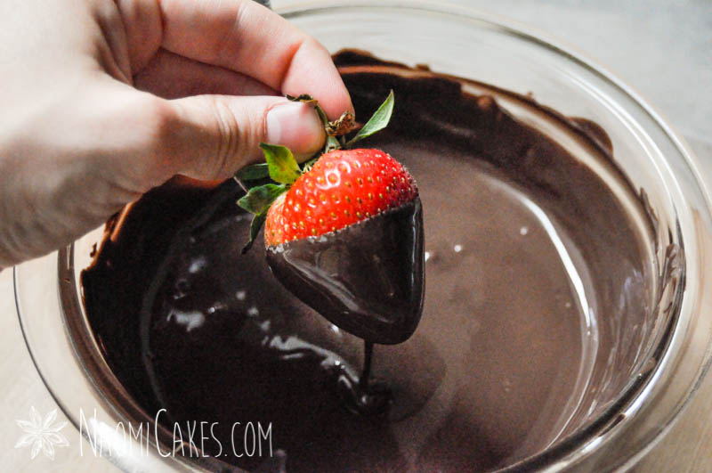 hand lifting a freshly dipped strawberry out of chocolate