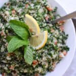 an overhead view of a bowl of quinoa tabbouleh with lemon and fresh mint on top on a white background