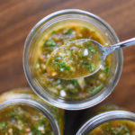 a spoonful of fresh green chile with a wooden background and 3 jars
