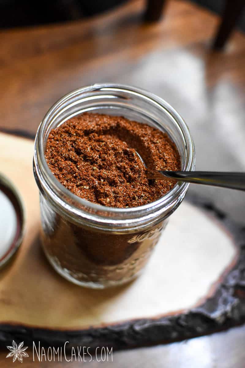 a mason jar with homemade taco seasoning on a wooden board with a spoon in it