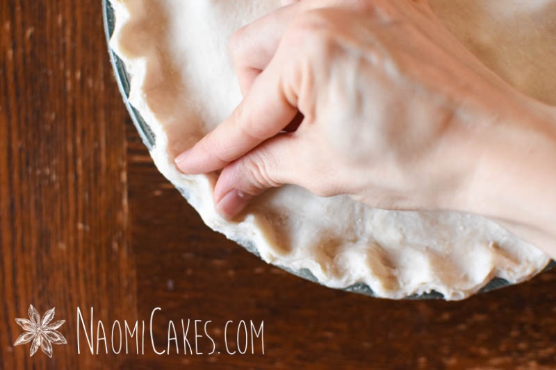 a hand fluting the edges of a pie on a wooden table