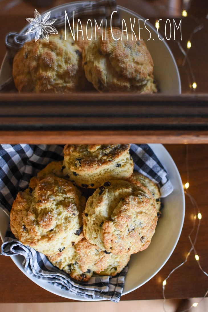bowl of currant scones reflecting in a glass display case with a checkered tea towel and fairy lights