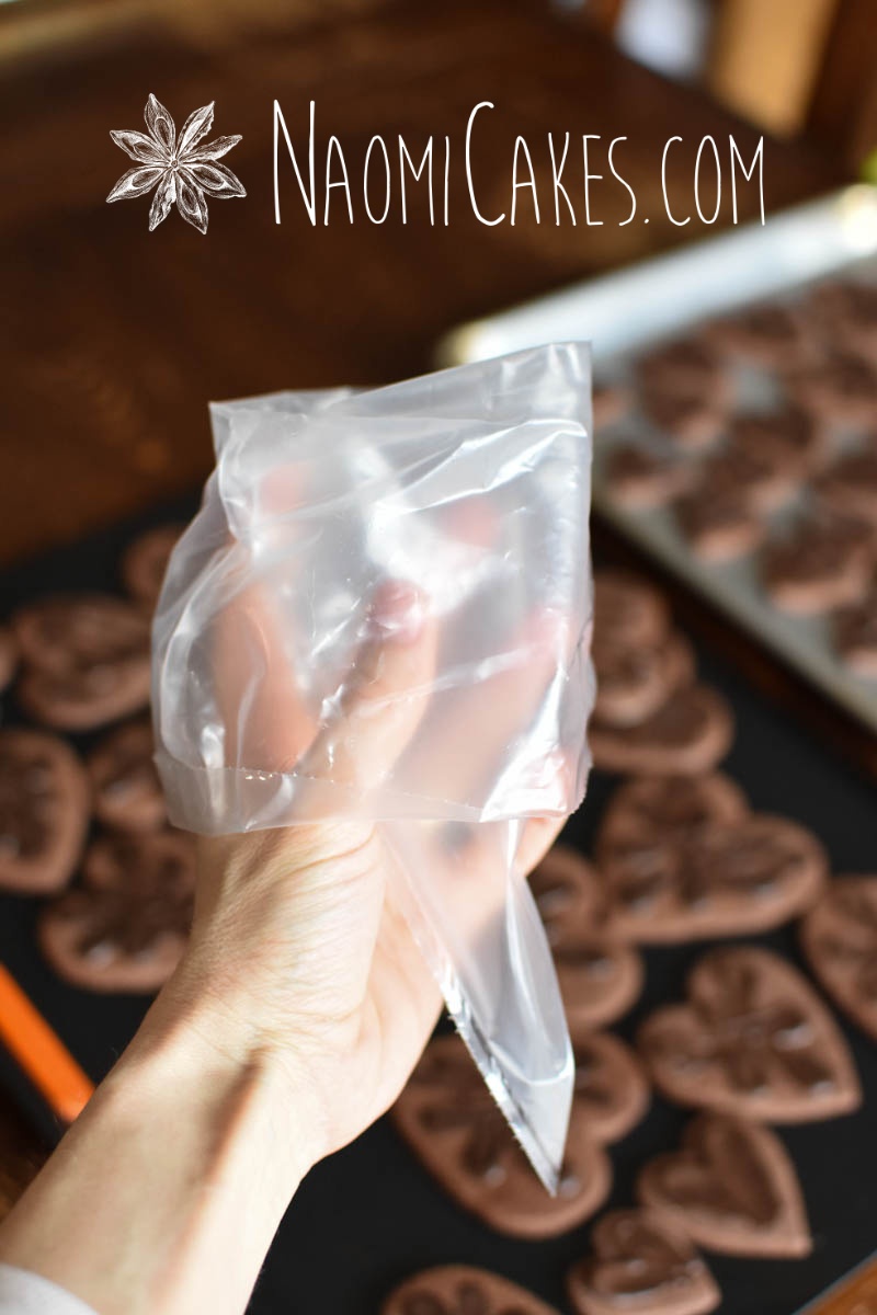 a hand holding a piping bag with a cuff with heart shaped chocolate cookies in the background