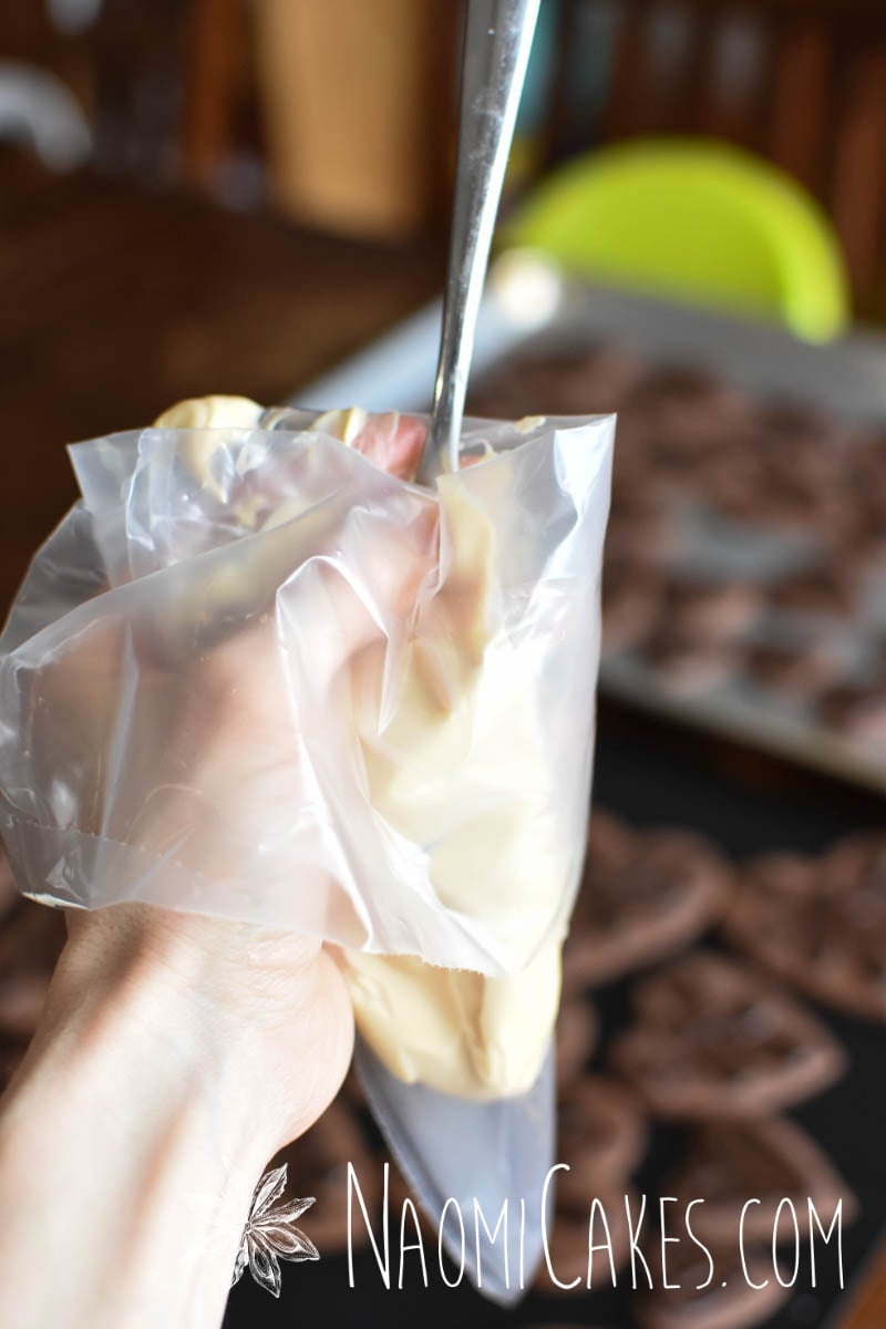 a hand holding a piping bag and filling the bag with melted white chocolate