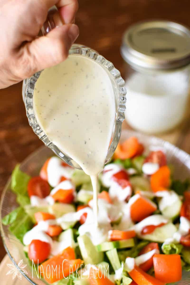 glass pitcher of creamy yogurt salad dressing pouring over a garden salad