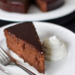 a white plate with Sachertorte and whipped cream