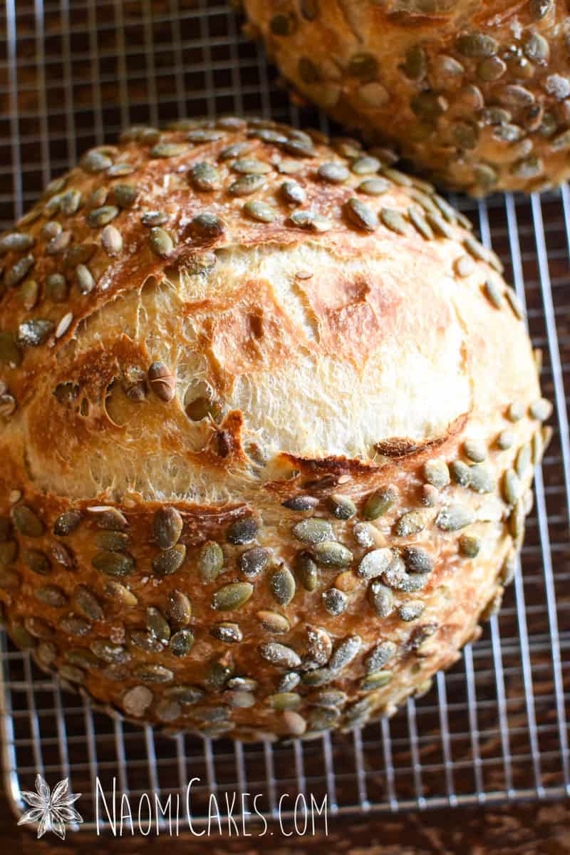 close up of a sourdough pumpkinseed bread loaf on a cooling rack