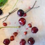 a cookie sheet with several sour cherries, bobby pins, cherry leaves, stems, and pits