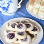 gluten-free shortbread jam thumbprint cookies on a plate on a table with a tea pot and sandwiches in the background