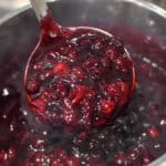 a ladle full of fresh made cherry pie filling over a pot of pie filling on the stove
