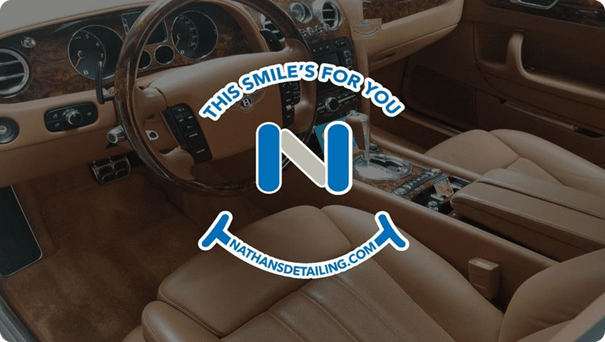Photo of a luxury car’s tan leather interior with a blue and white Nathan’s Detailing logo in the center and the text “This smile’s for you” and “nathansdetailing.com.”.