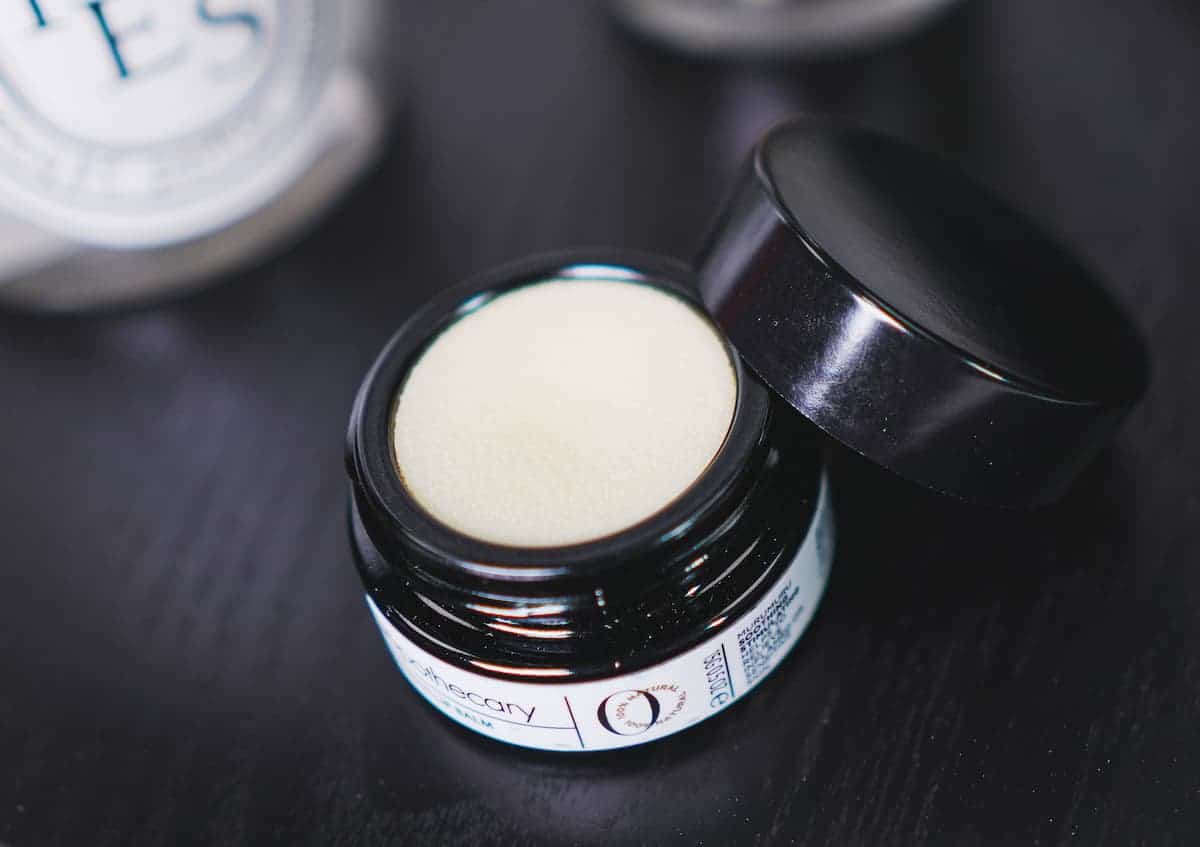 image of the ilapothecary lip balm opened with the lid slanted off to the side. the balm is an off-white and balmy texture and color.