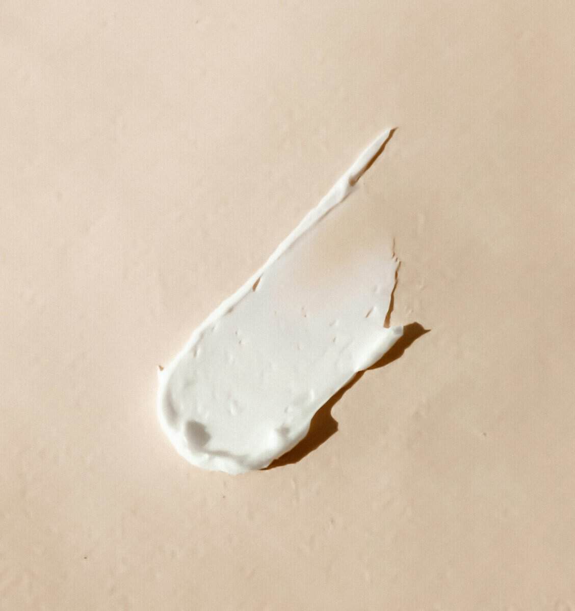 A swatch of white moisturiser on a soft beige background