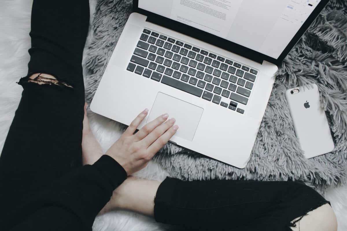 Overhead view of a woman in black jeans sitting on a white floor, working at a laptop
