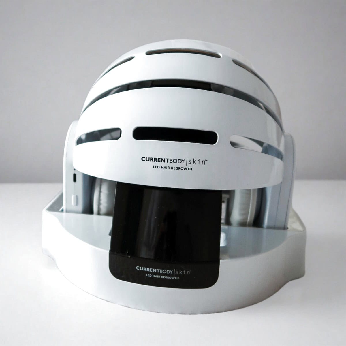 CurrentBody LED Hair Growth Helmet on its charging base on a white table