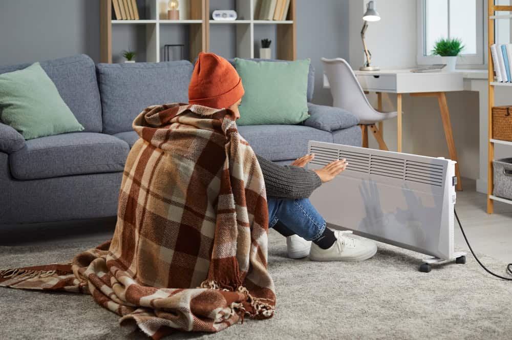 Cozying up by the heater on a chilly day, wrapped in a warm blanket and a cozy hat.