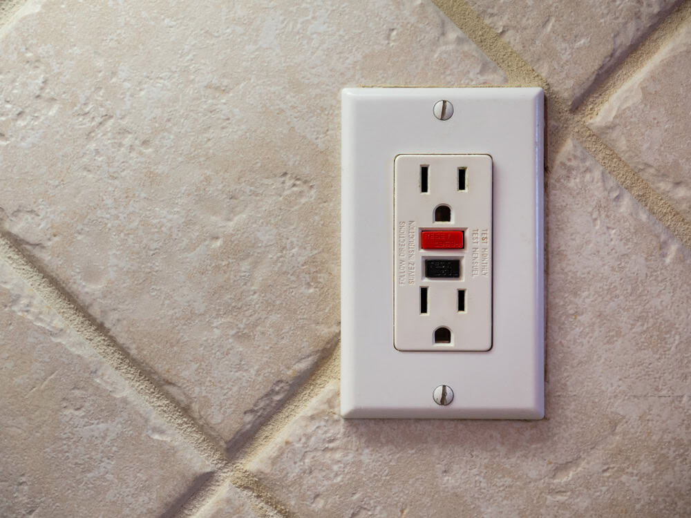 A GFCI electrical outlet installed on a tiled kitchen wall.