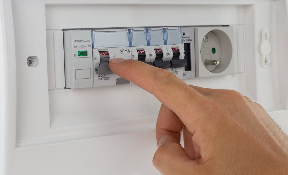 A person resets a circuit breaker switch in a modern electrical fuse box.