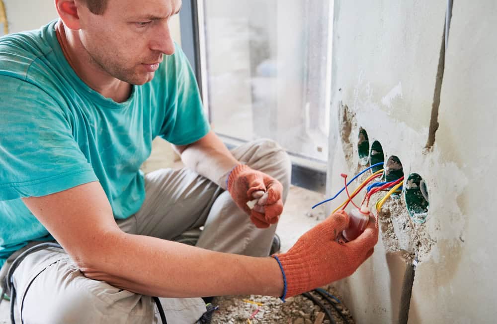 An electrician carefully installs wiring in a wall during a home renovation project.