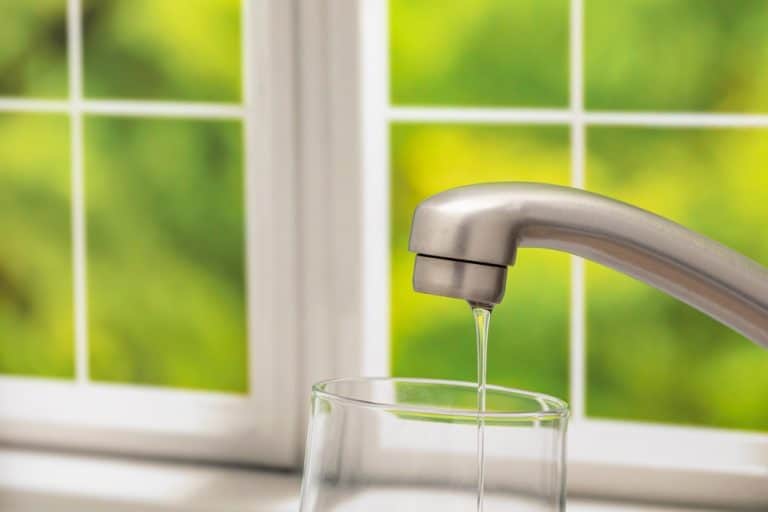 Tap water filling a glass at a sunlit kitchen window