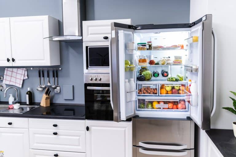 Modern white kitchen featuring an open stainless steel refrigerator stocked with fresh produce, alongside built-in appliances and sleek black countertops.
