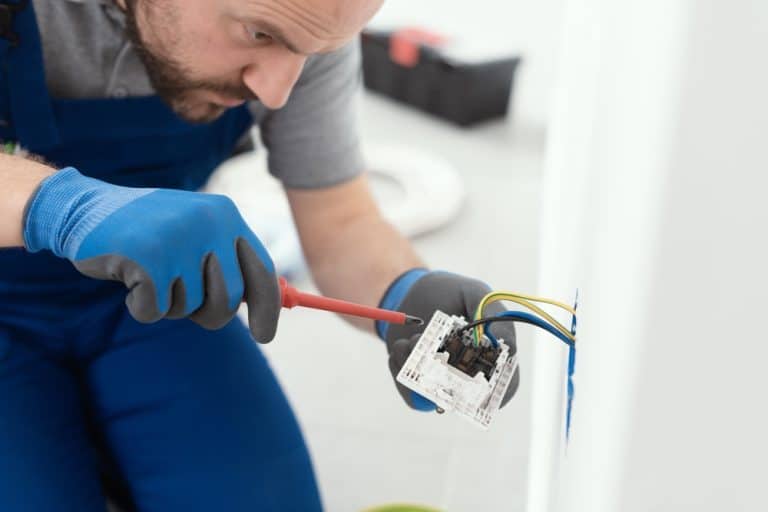 Electrician carefully wiring a wall socket with precision tools and safety gloves.