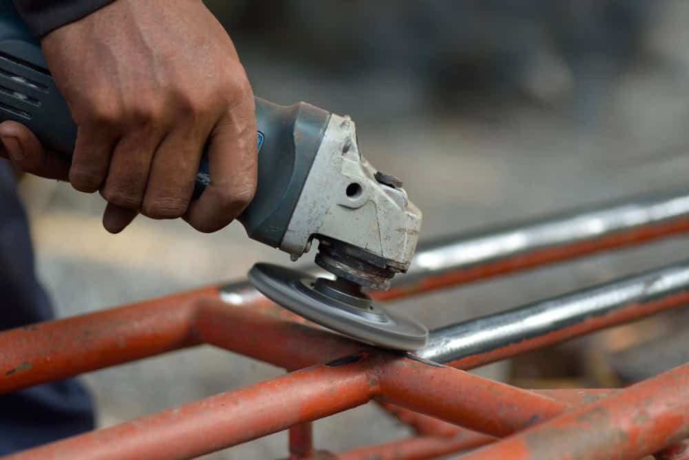 A worker uses an angle grinder to polish metal pipes, transforming rusted steel into a smooth, shiny surface.