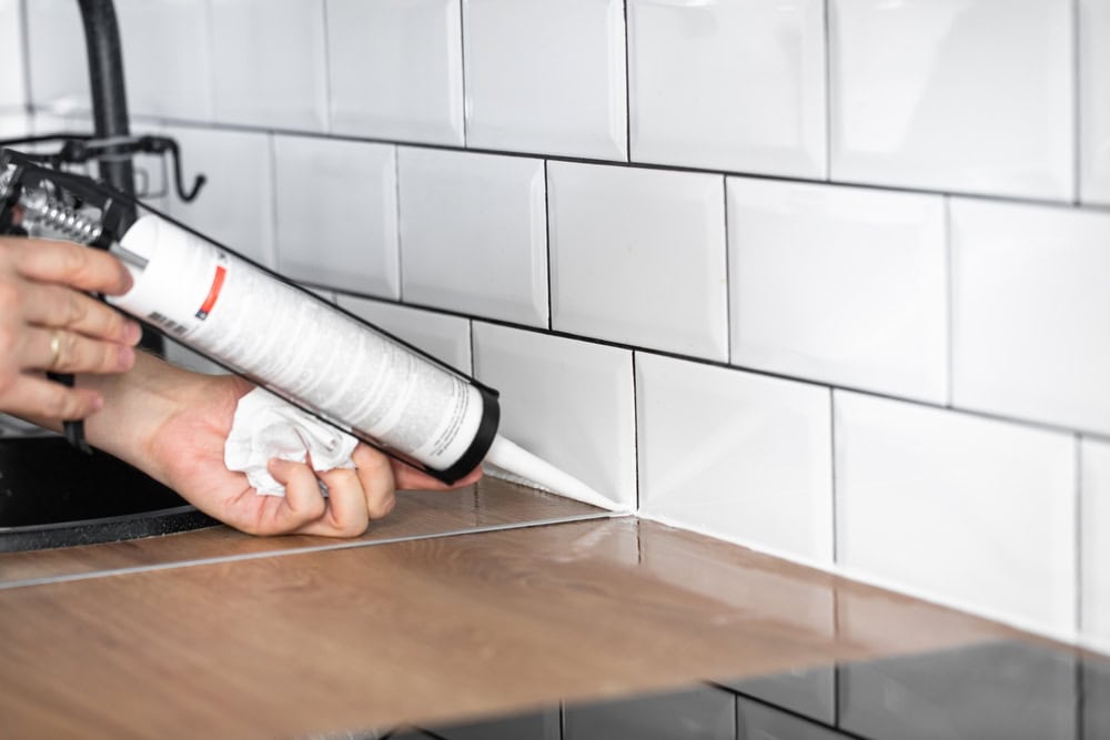 Applying caulk to seal the kitchen backsplash for a clean, professional finish.