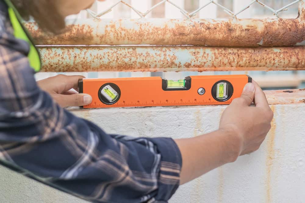 A worker uses a spirit level to ensure the alignment of a rusted metal structure.