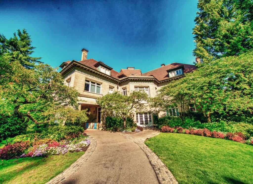 A charming mansion surrounded by vibrant gardens and a winding cobblestone path under a clear blue sky.