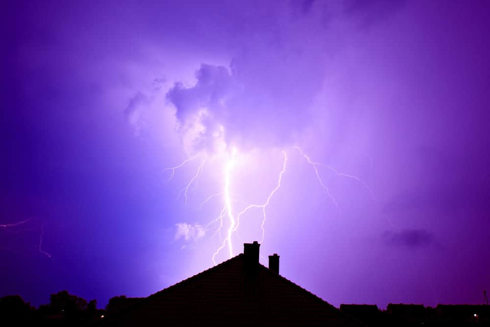 Lightning strikes dramatically over rooftops under a purple stormy sky.