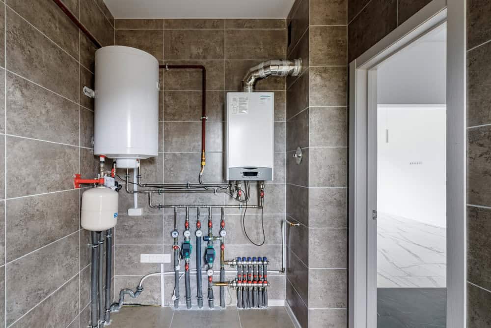Modern home heating system with boiler and water heater in a neatly tiled utility room.