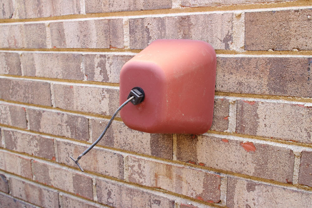 Weathered electrical outlet cover on a brick wall, with a frayed cord sticking out.