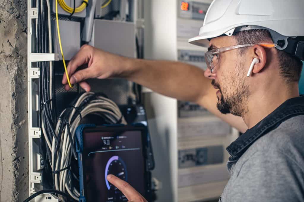 Network technician performs speed test while installing fiber optic cables, equipped with safety gear and using a tablet to monitor connection performance.
