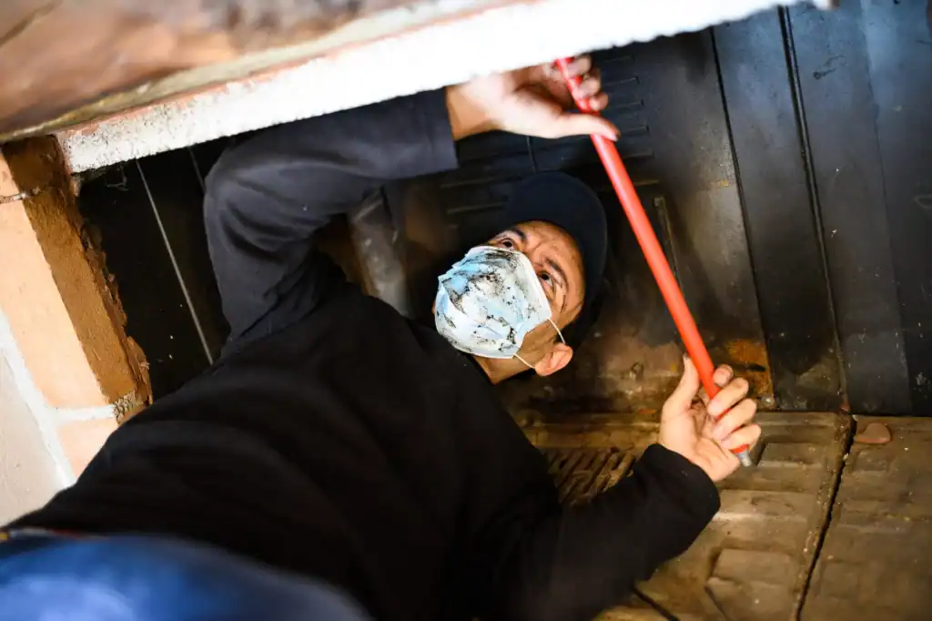 A chimney sweep in a mask meticulously cleans a fireplace.