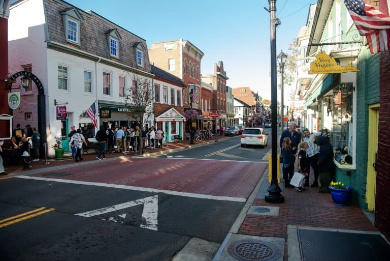 Shoppers walk a brick sidewalk past storefronts on a historic street in Leesburg, Virginia