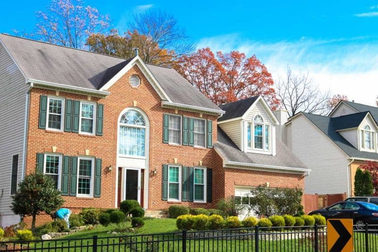 A two-story brick colonial house with green shutters, next to a neighboring home, in an Annandale, Virginia neighborhood.
