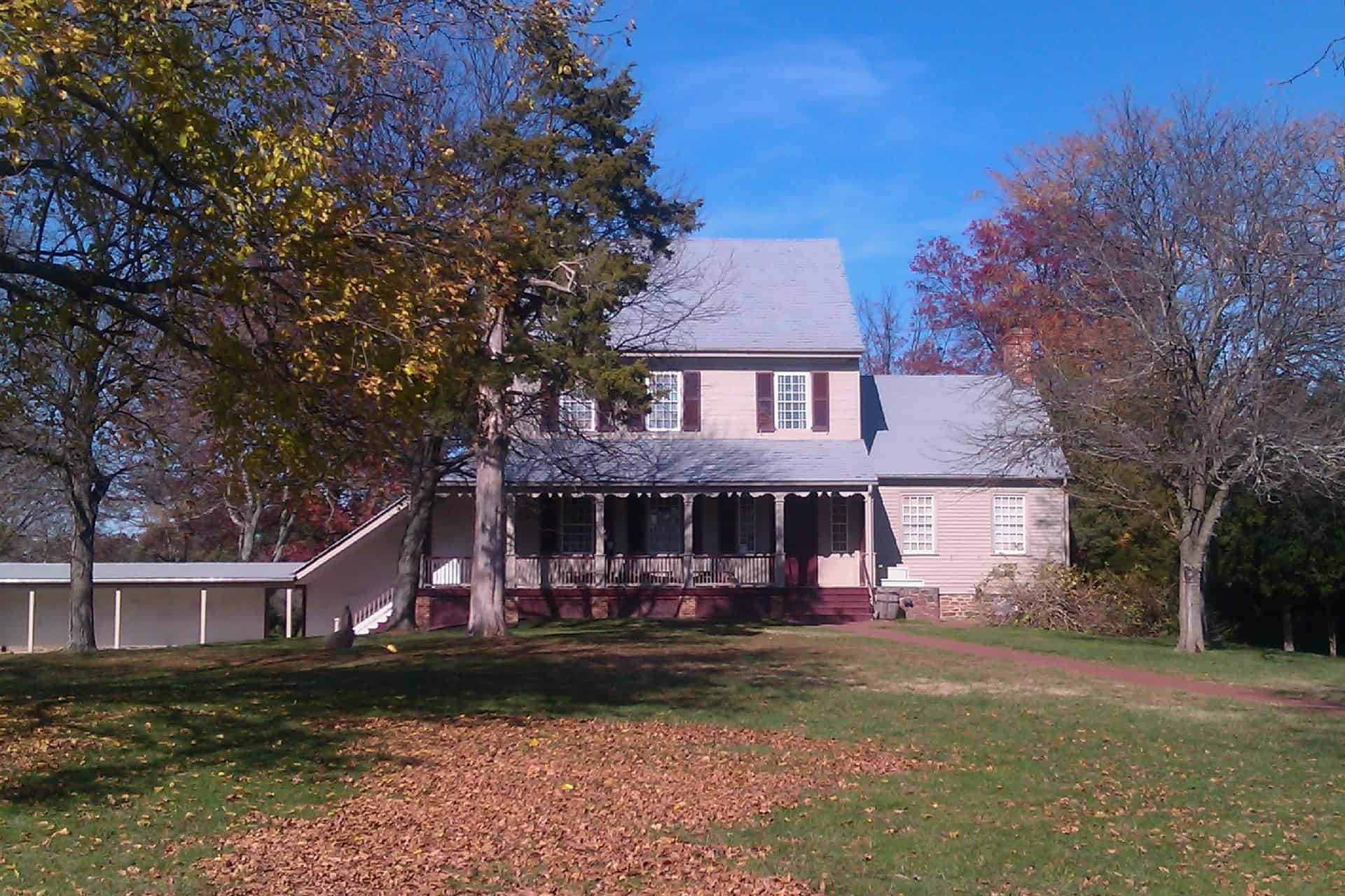 A two-story colonial house with a full-width porch and red shutters, surrounded by autumn leaves in Chantilly, Virginia.