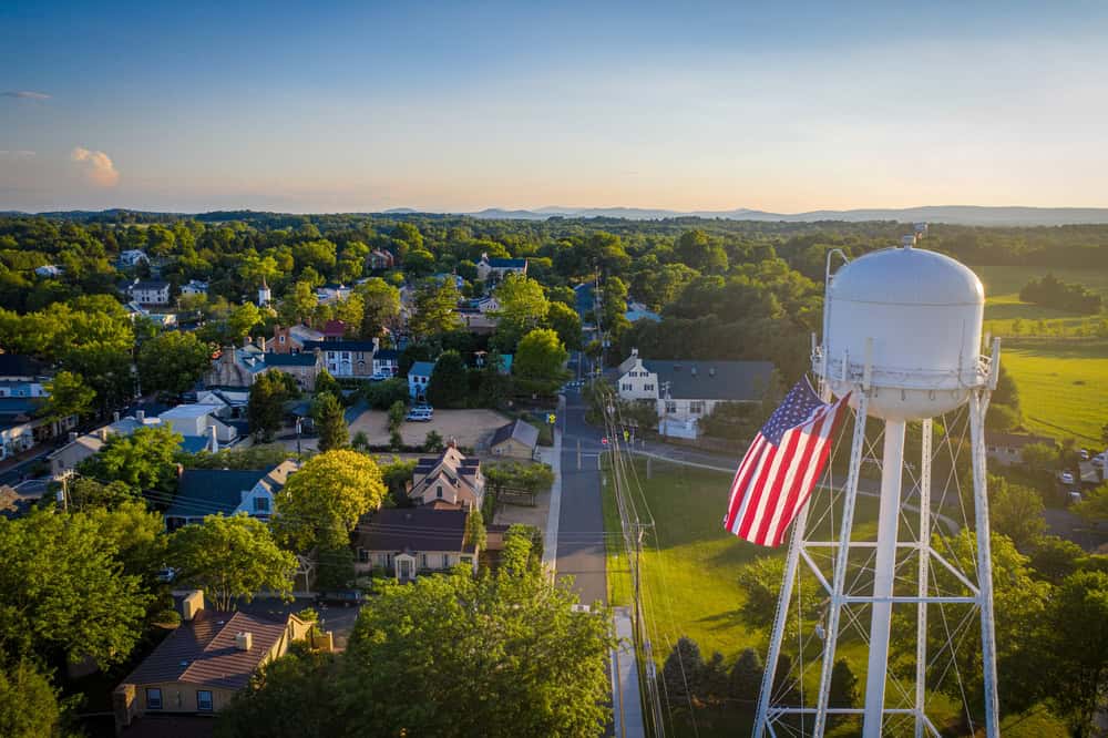 A water tower draped in an American flag rises over rooftops and trees in a Loudoun County town at dusk