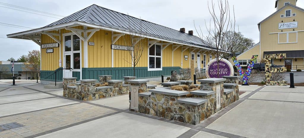 The yellow and green Purcellville Train Station building sits behind a paved plaza in Virginia
