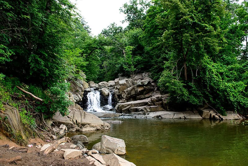 A small waterfall tumbling over rock ledges into a green pool at Scott's Run Nature Preserve in McLean, Virginia.