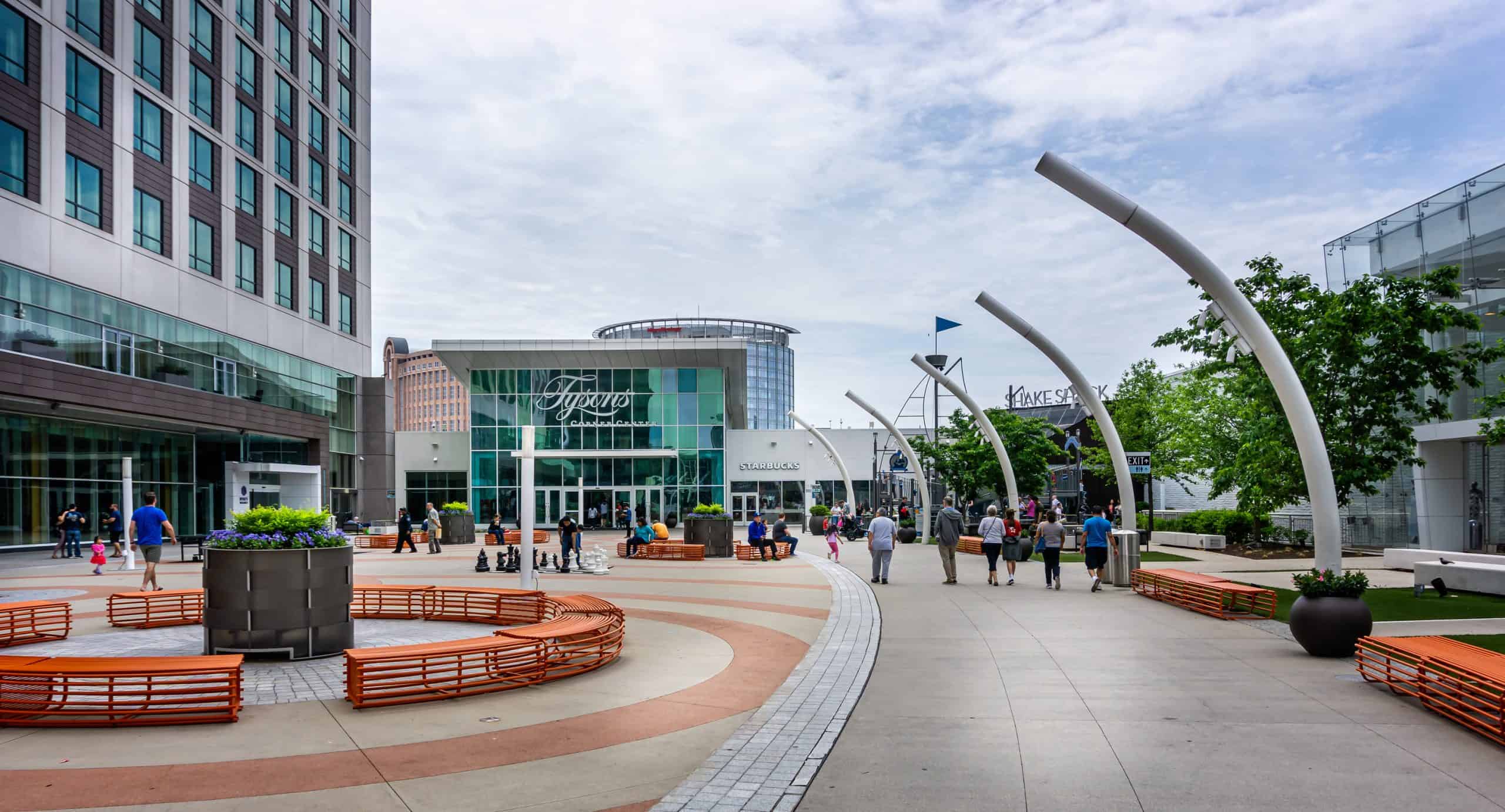 The plaza outside Tysons Corner Center mall, with people walking near curved metal sculptures and a Starbucks storefront.