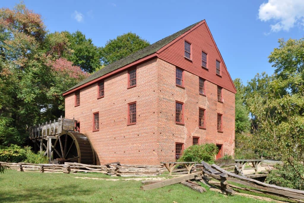 The red brick colonial era Colvin Run Mill building with a wooden water wheel, near Great Falls, Virginia.