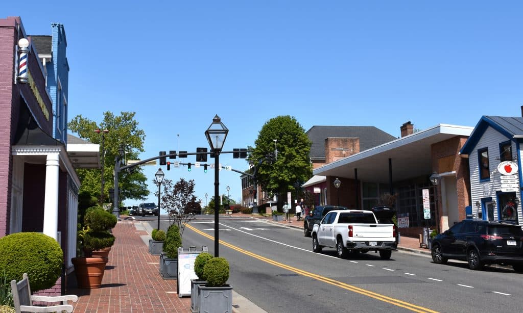 Main Street in Fairfax, Virginia lined with historic storefronts, a barber pole, and street lamps on a sunny day.