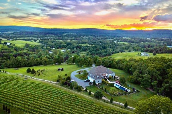 An aerial view at sunset of a large white house and pool surrounded by vineyard hills near Round Hill, Virginia
