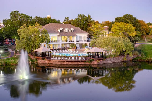 A resort-style clubhouse with a pool, cabanas, and a lit fountain on a lake at dusk in Centreville, Virginia.