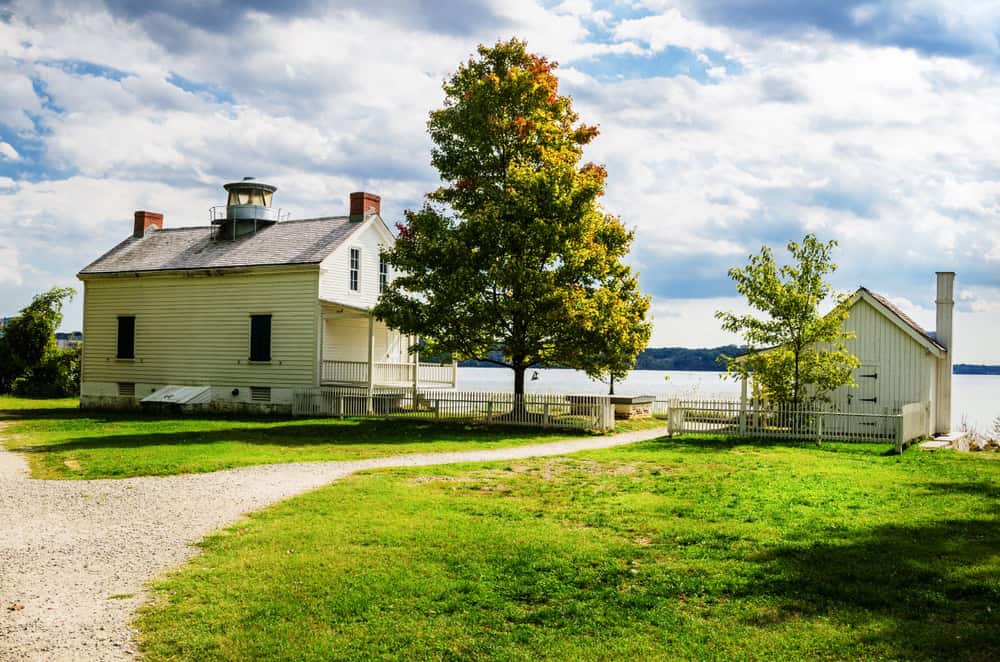 A small white clapboard cottage with a lighthouse lamp on its roof, beside the Potomac River in Alexandria, Virginia.